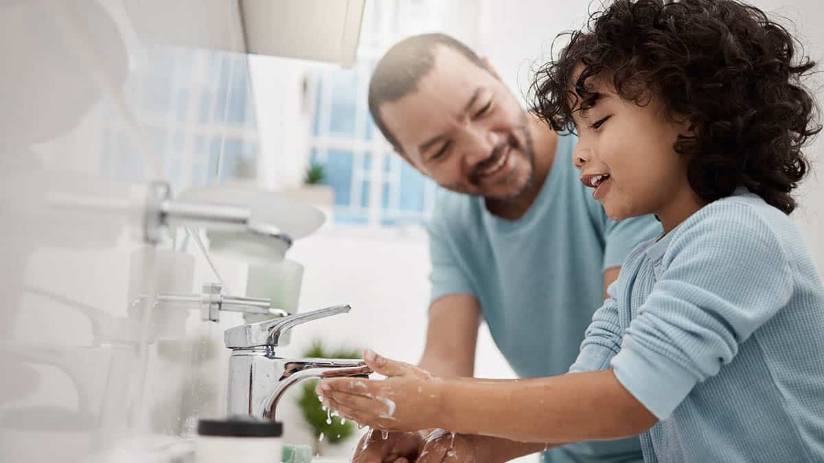 Father and son washing their hands underneath a running sink faucet