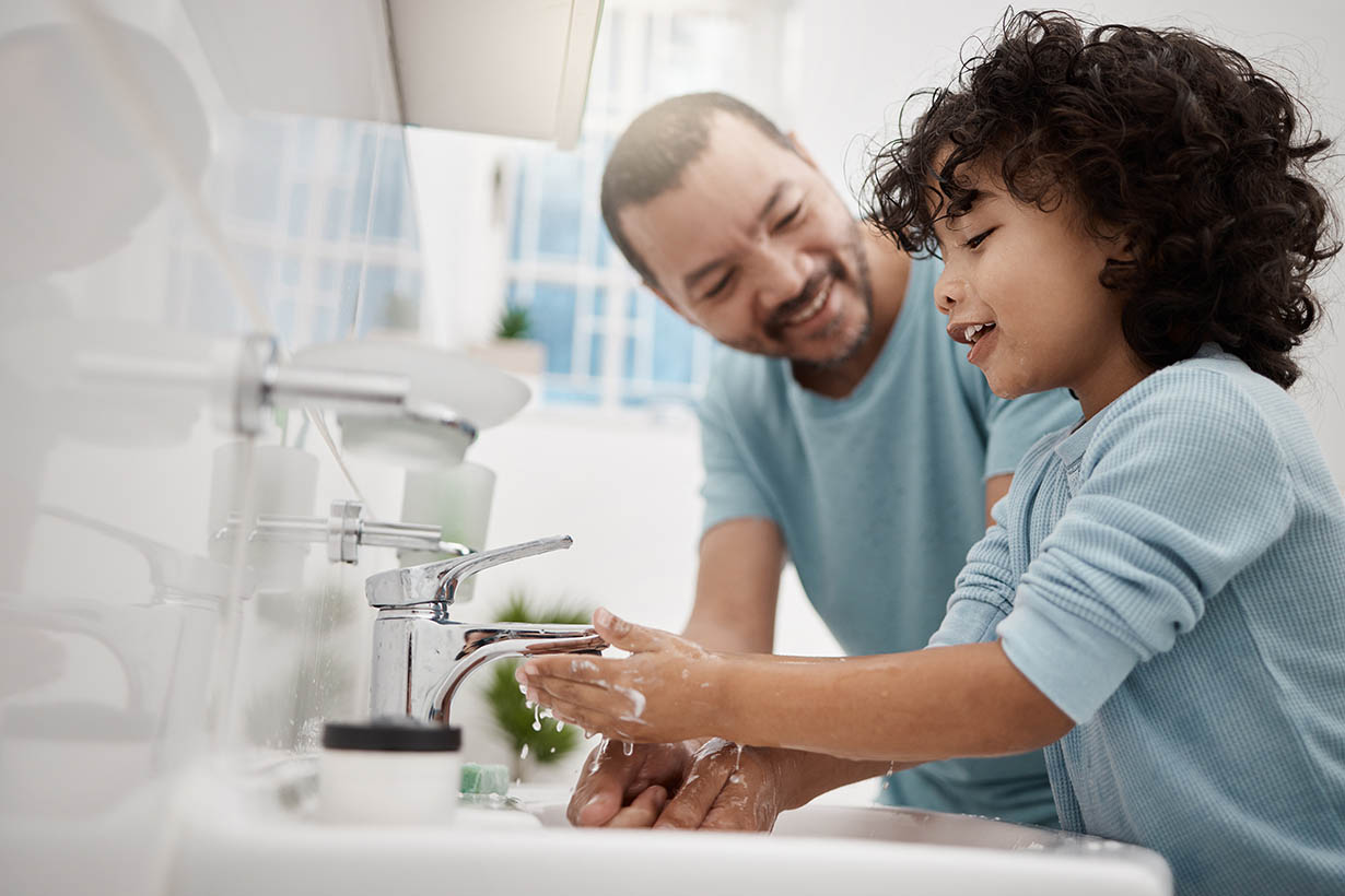 Picture of a father helping his son wash his hands and face at a tap in a bathroom